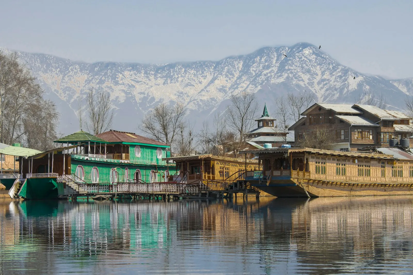 Green and brown wooden house on lake near snow covered mountain during daytime Houseboats on Dal Lake in Srinagar, the summer capital of Jammu and Kashmir: Kash